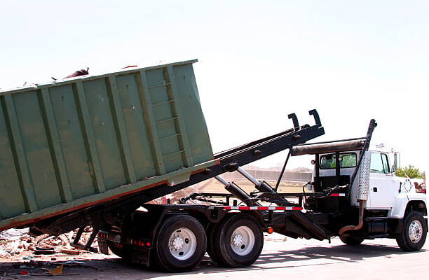 A dumpster loaded with trash is unloaded by a heavy duty truck.